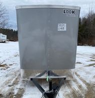 A silver enclosed cargo trailer parked on a snowy, muddy lot.