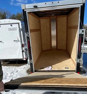 Empty wooden trailer with open rear door on snowy ground.