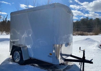 White enclosed utility trailer parked on snow under a blue sky.