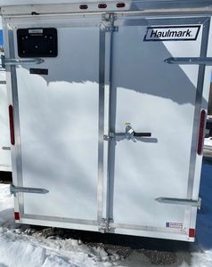 Rear view of a white Haulmark trailer with double doors in snowy conditions.