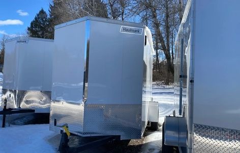 Several silver Haulmark trailers parked on snowy ground under a clear blue sky.