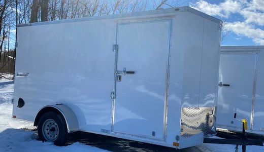 White enclosed cargo trailer parked on snow-covered ground under blue sky.