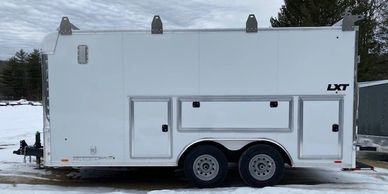 White enclosed trailer with dual axles parked on snowy ground.