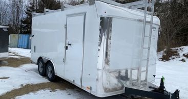 White enclosed trailer with dual axles parked on snowy ground.