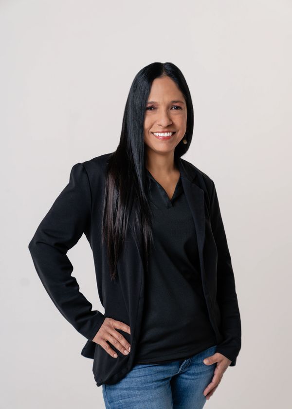 Smiling woman in black blazer and jeans posing confidently.