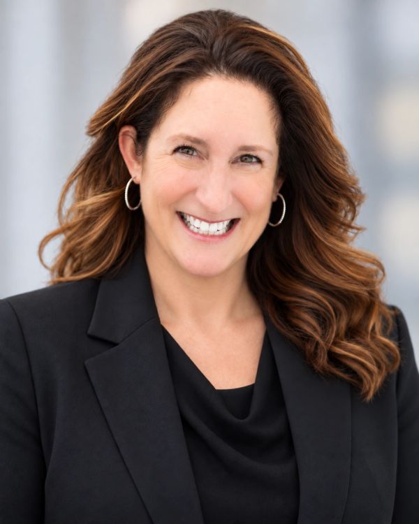 Smiling woman with curly hair wearing a black blazer.