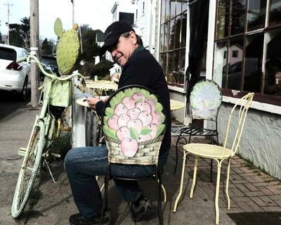 Man sitting on a decorated metal chair on a sidewalk.