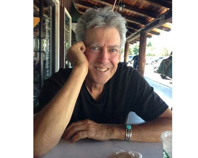 Smiling man sitting at a table in a rustic outdoor setting.