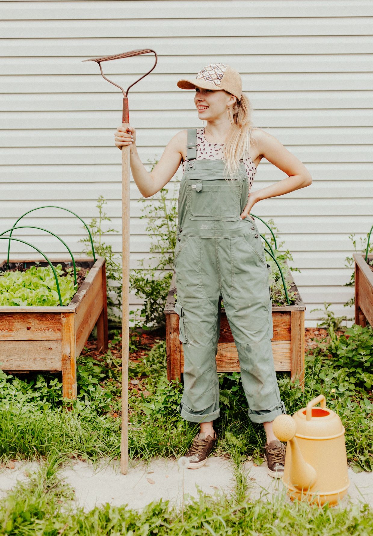 Woman gardener in overalls holding a rake, standing between raised garden beds.