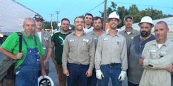 Group of nine workers posing outdoors, some wearing uniforms and hard hats.
