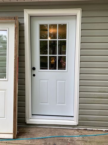 A white door with glass panes installed on a house with beige siding.