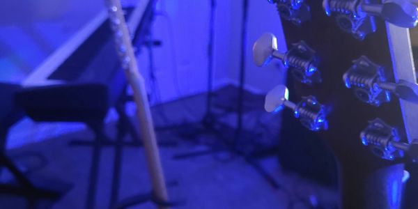 Close-up of guitar tuning pegs with a keyboard and guitar in blue-lit room.