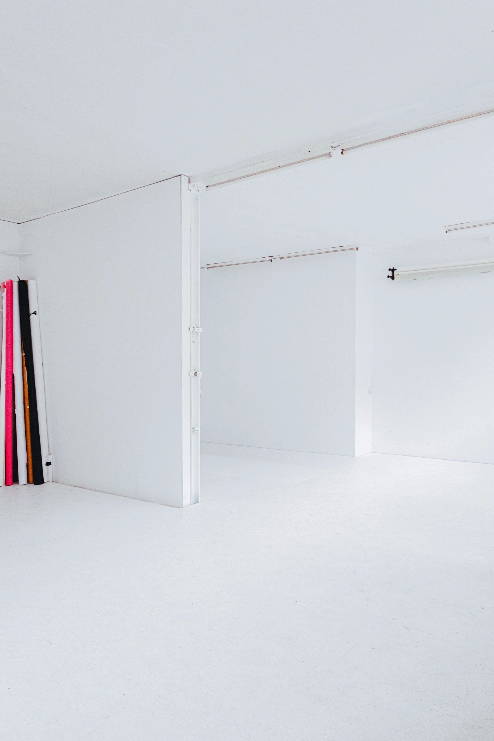 Minimalist white room with colored rolls of paper in the corner.