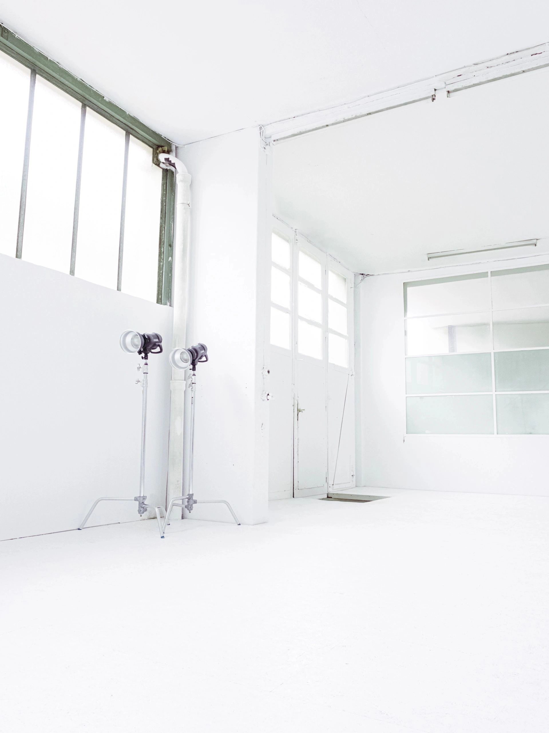 Bright, empty white room with studio lights and large windows.