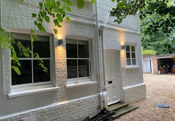 White brick house exterior with lit wall lights and greenery.