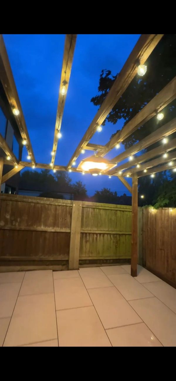 Cozy outdoor patio with string lights under a wooden pergola at dusk.