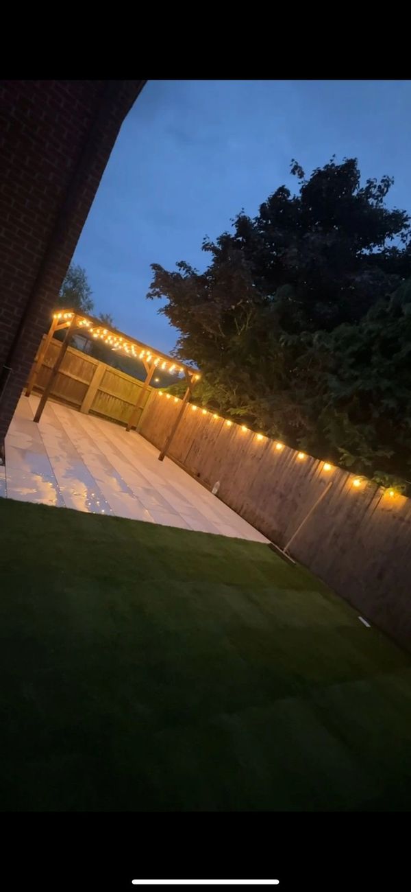 Backyard patio with string lights and a wooden pergola at dusk.