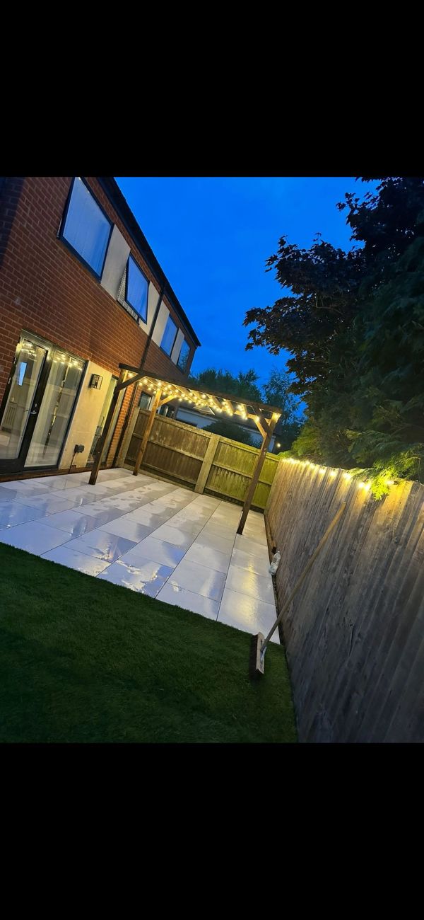 Cozy backyard patio with string lights under a wooden pergola at dusk.