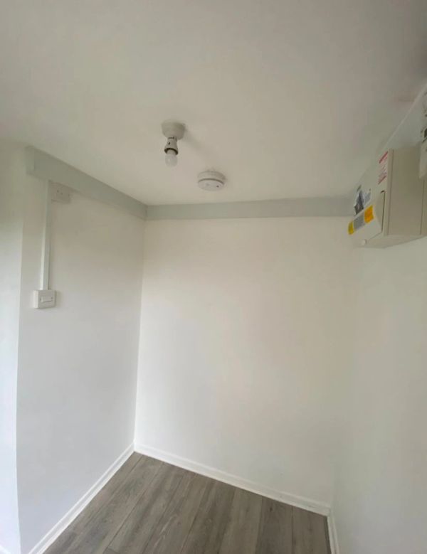 Empty white room with wooden floor and ceiling fixtures.