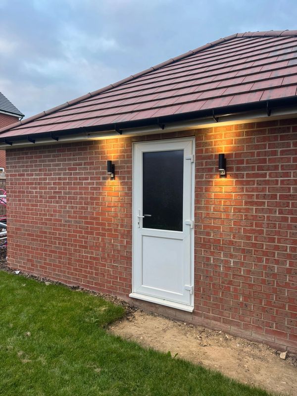 White door on a brick building illuminated by two wall lights.