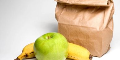 Brown paper lunch bag with a green apple and two bananas.