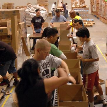Volunteers packing boxes in a warehouse assembly line.
