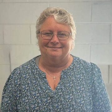 Smiling elderly woman with glasses and curly gray hair in a blue floral top.
