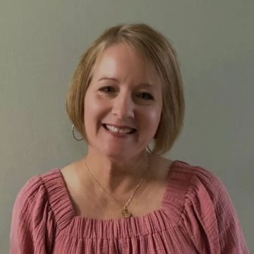 Smiling woman in a pink blouse against a plain background.