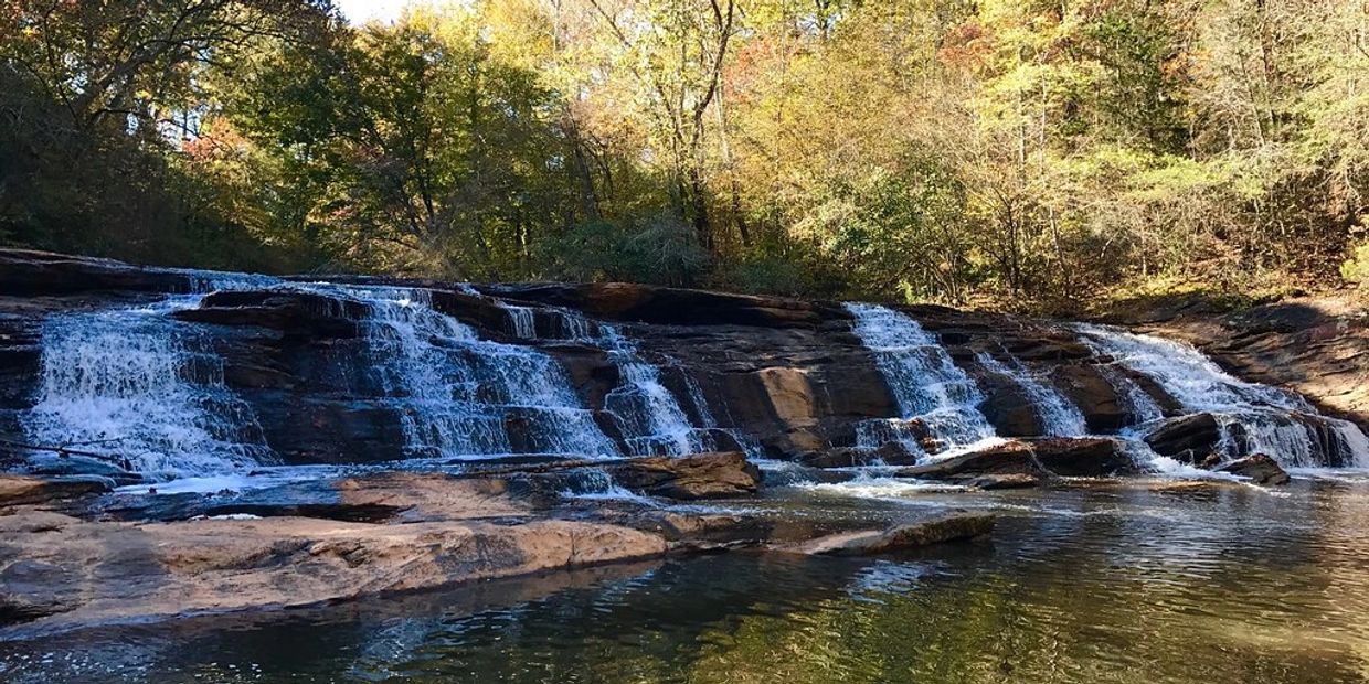 Wide waterfall flowing over rocks surrounded by trees.