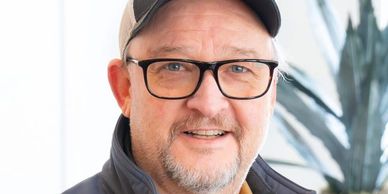 Smiling man wearing glasses and a cap.