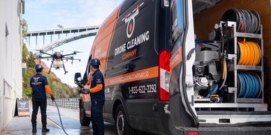 Workers operate a drone to clean a large surface near a cleaning company van.