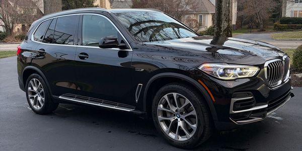 A shiny black BMW SUV parked on a driveway with houses and trees in the background.
