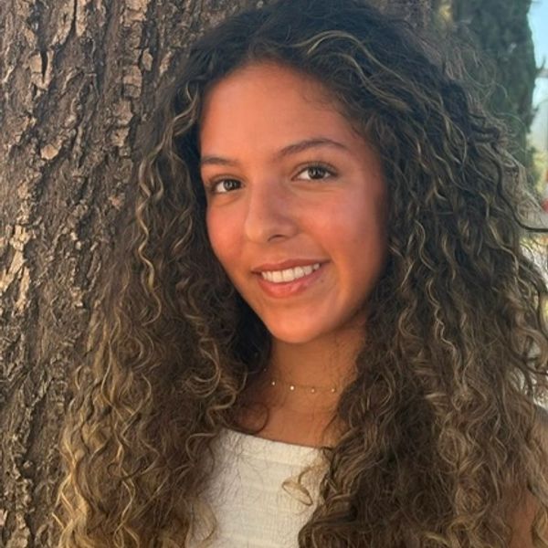 Smiling young woman with curly hair by a tree.