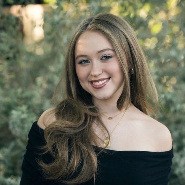 Young woman smiling with long hair and off-shoulder top outdoors.