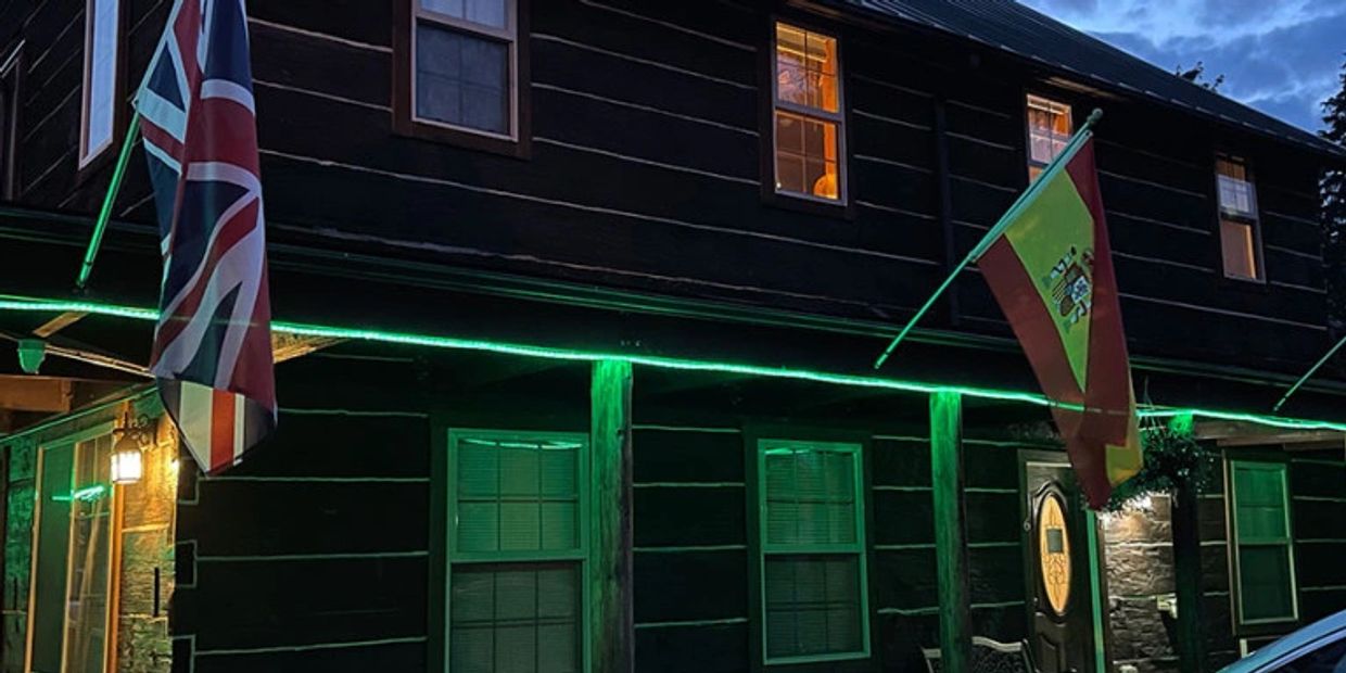 A dark building decorated with British and Spanish flags illuminated by green lights at night.
