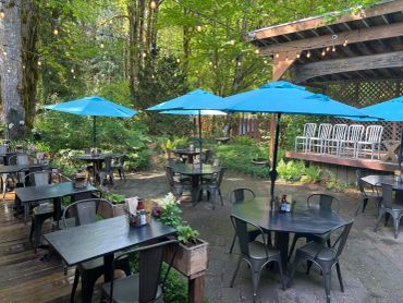 Outdoor cafe seating with blue umbrellas surrounded by greenery.