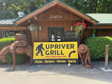 Wooden building with Upriver Grill sign and Bigfoot statues.