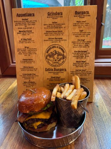 Juicy double cheeseburger with bacon and fries in a metal bucket on a wooden table.