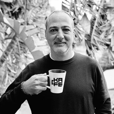 Man smiling while holding a coffee mug with 'KAFE' text.
