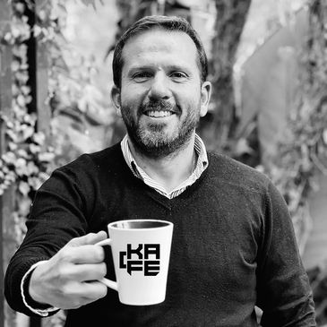 Man smiling and holding a coffee mug with 'KAFE' text.