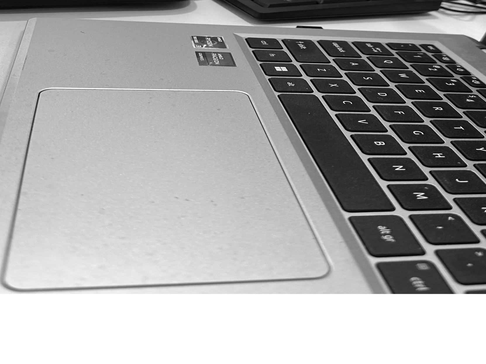 Close-up of a laptop keyboard and trackpad with tools and keyboard in the background.