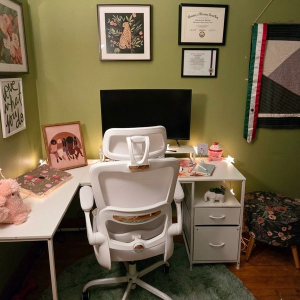 Cozy green-walled workspace with white desk, ergonomic chair, and floral decor.