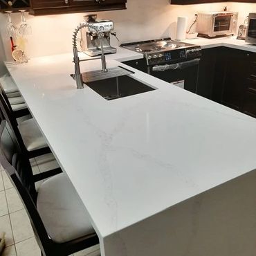Modern kitchen with white marble countertop and black chairs.