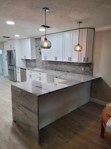 Modern kitchen with white cabinets, marble countertops, and pendant lights.