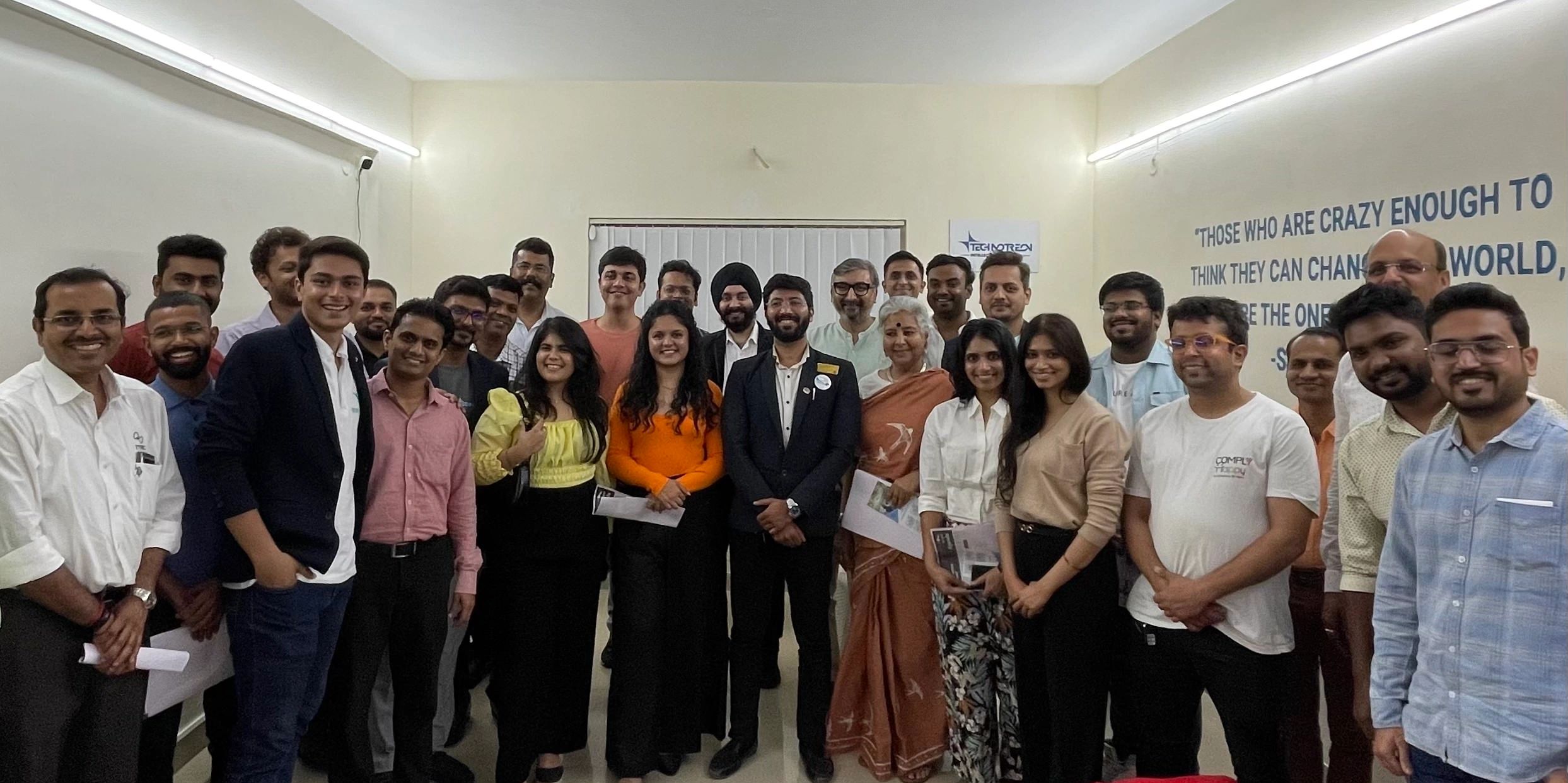 Group photo of diverse professionals smiling in a well-lit room with motivational quote on the wall.
