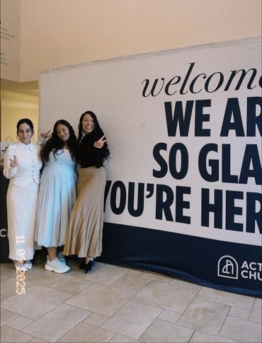 Three women standing happily in front of a welcome sign at a church.
