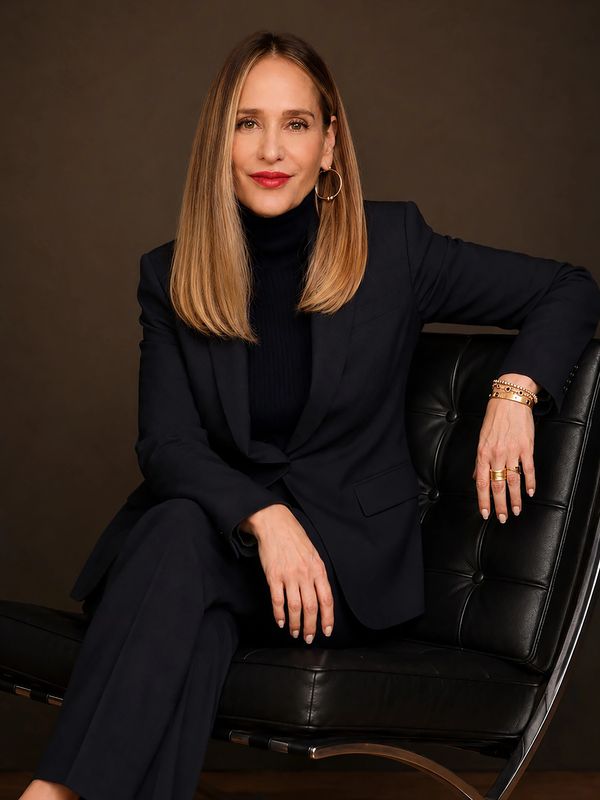 Confident woman in a dark suit sitting on a black leather chair, smiling warmly.