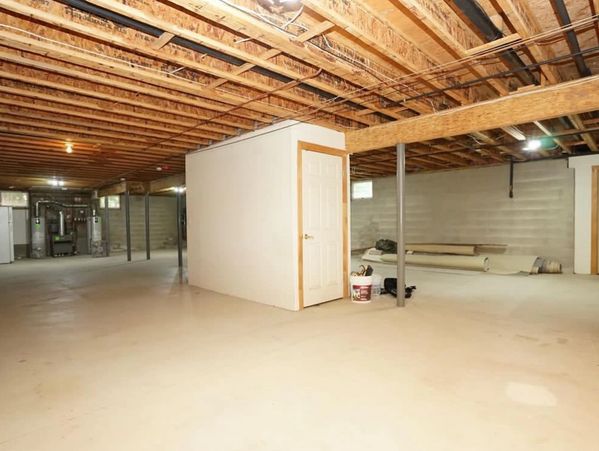 Unfinished basement with exposed ceiling beams, support columns and concrete floor before renovation.