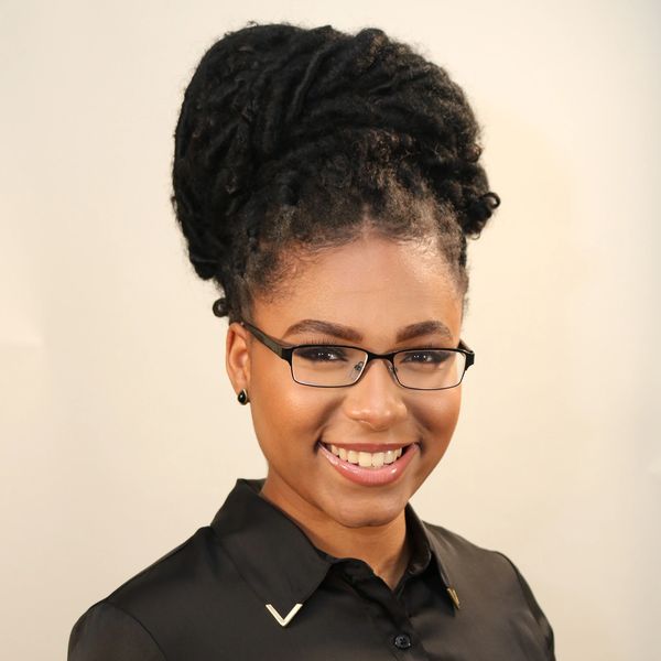Smiling woman with glasses and black shirt posing against a plain background.