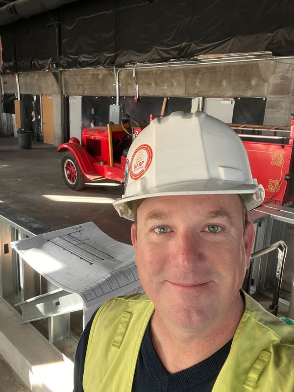 Man in hard hat and safety vest at construction site with vintage red fire truck.